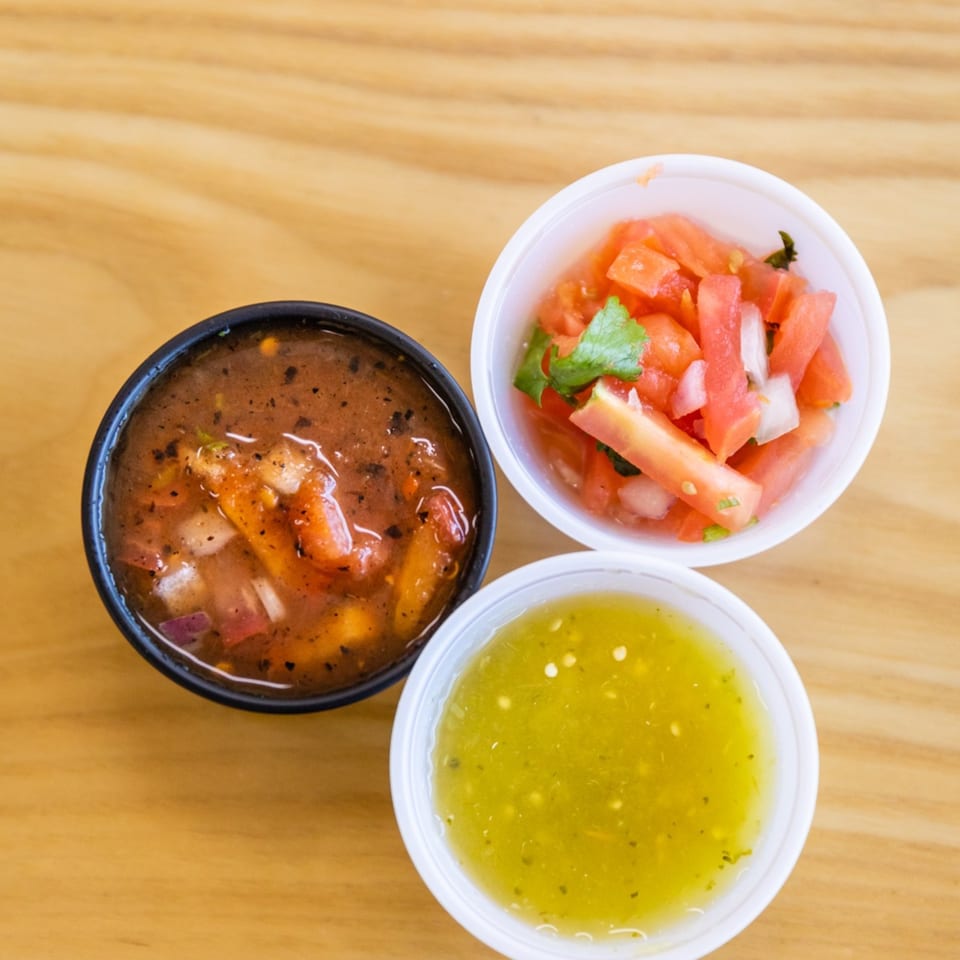 Three small cups of Mexican salsas: red salsa, pico de gallo, and green salsa.