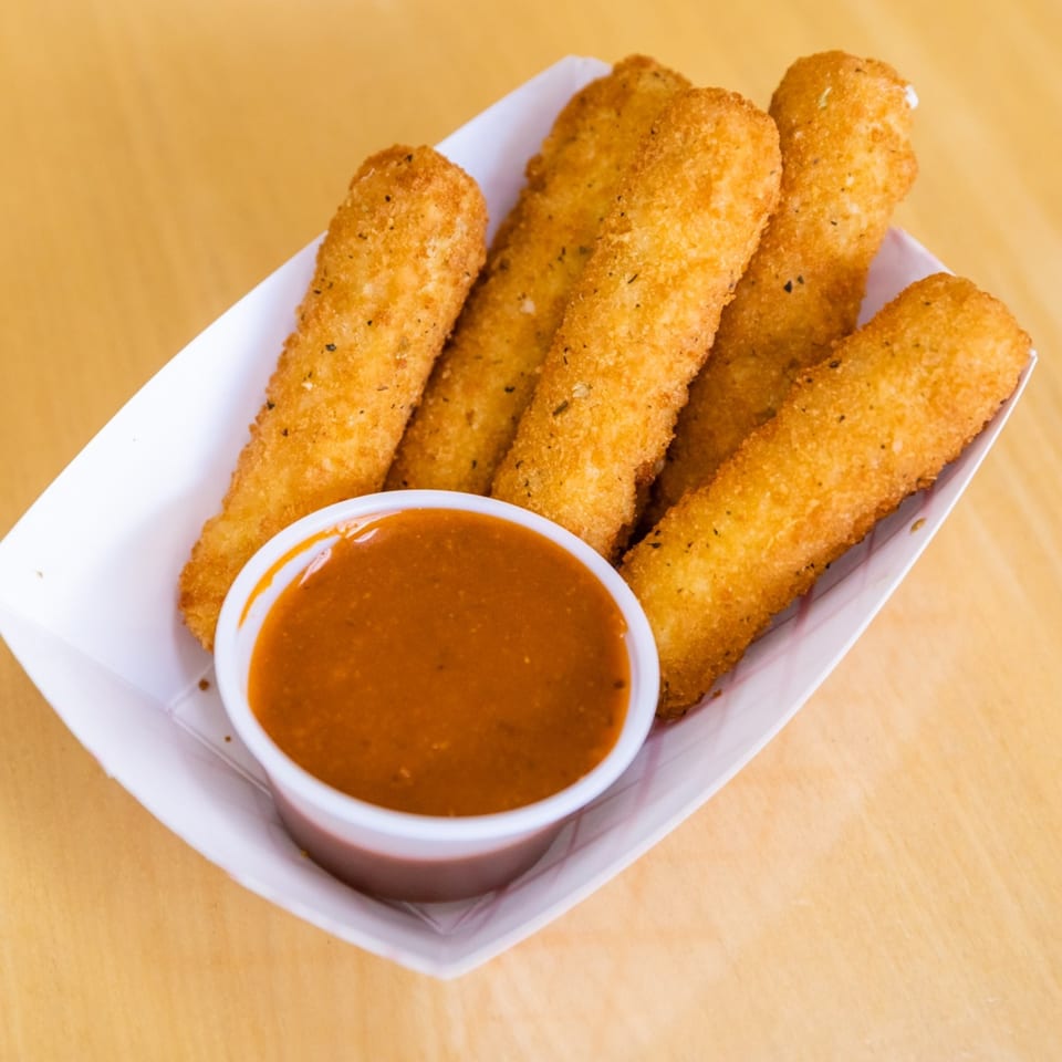 Golden-brown mozzarella sticks with a side of red dipping sauce in a white paper tray.