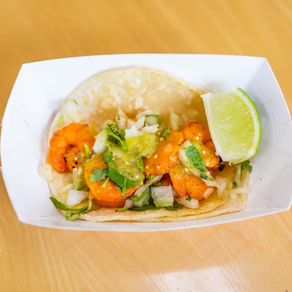 A shrimp taco from Blue Tortilla Fresh Mexican Grille, topped with salsa verde, onions, and cilantro.