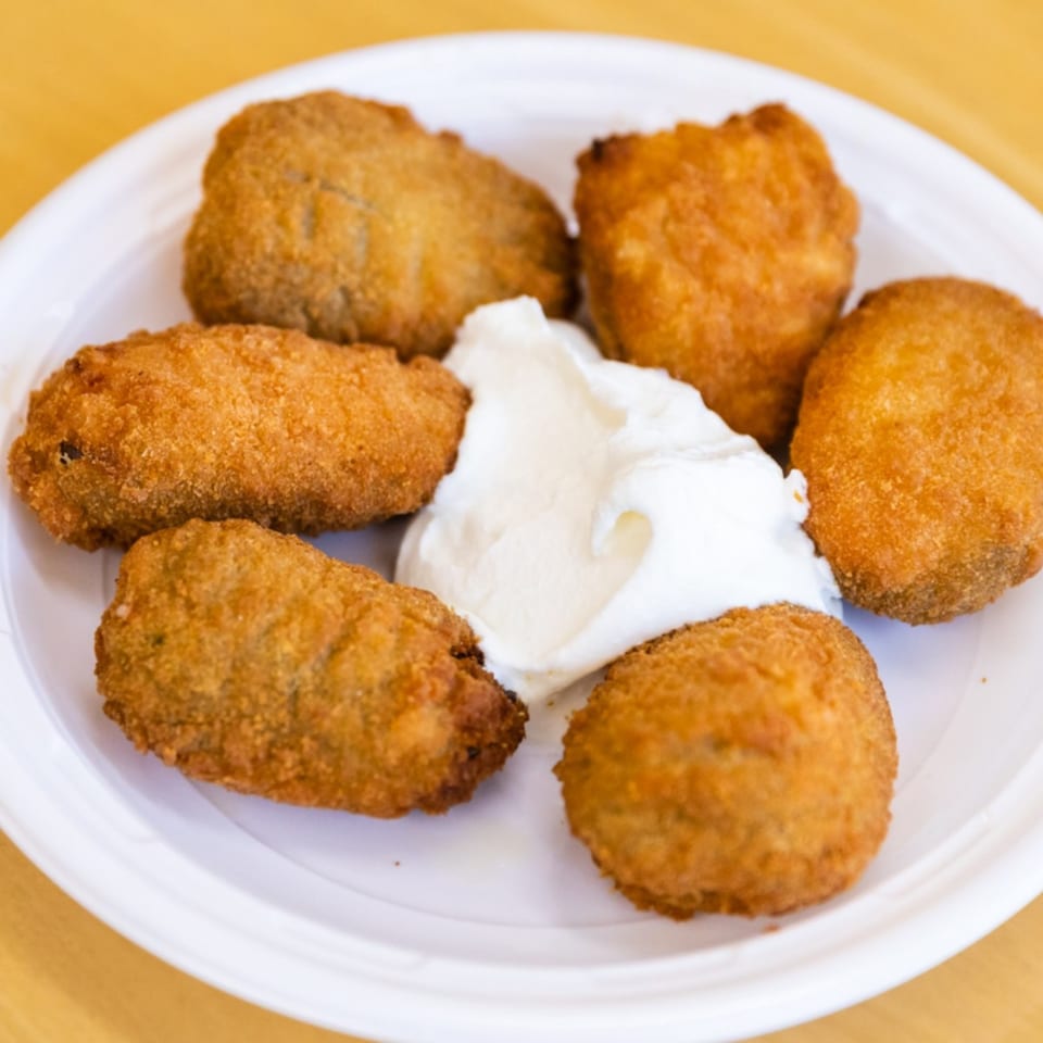 Six golden-brown fried Mexican appetizers with a dollop of white cream on a white plate.